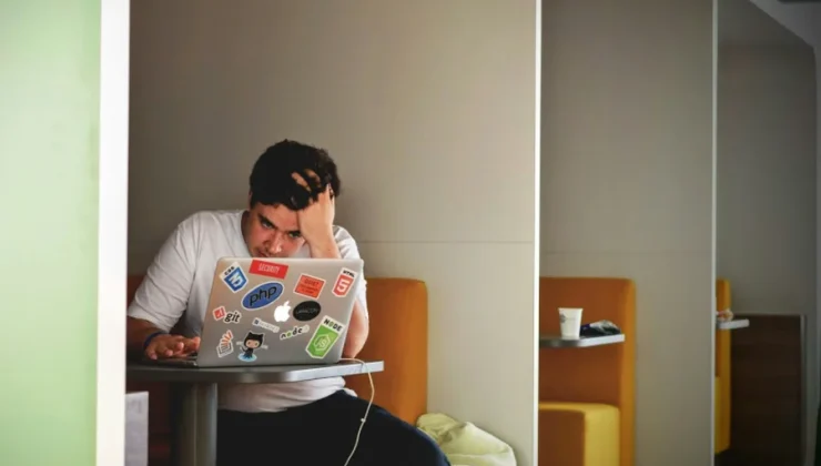 Man sitting in a booth, focused on a laptop covered in stickers.